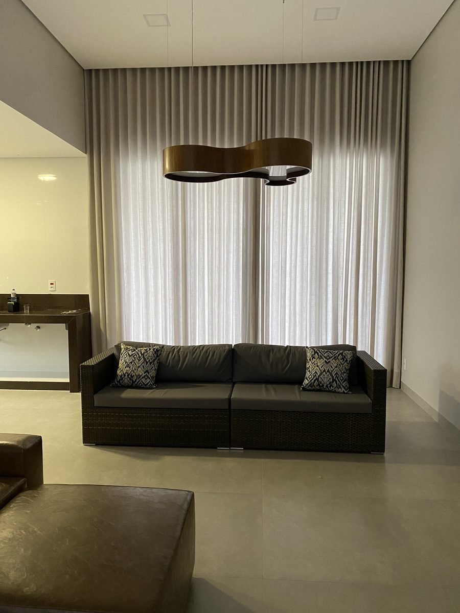 Sala de estar com sofá escuro e cortina wave clara em tecido leve